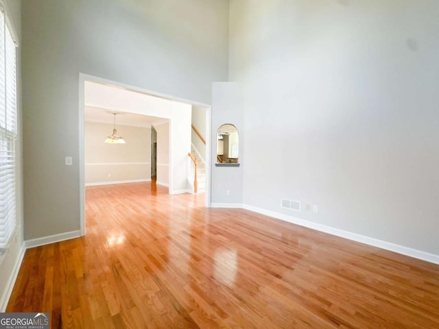 spare room with visible vents, light wood finished floors, baseboards, a towering ceiling, and stairs