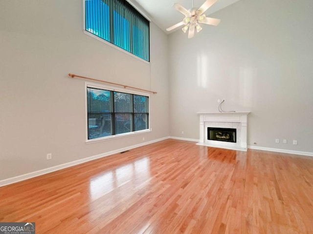 unfurnished living room with baseboards, a fireplace with flush hearth, wood finished floors, high vaulted ceiling, and a ceiling fan