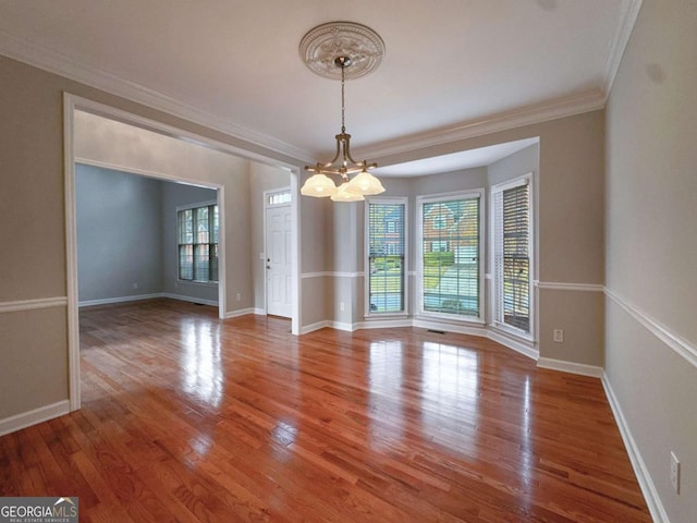 empty room featuring a chandelier, crown molding, baseboards, and wood finished floors