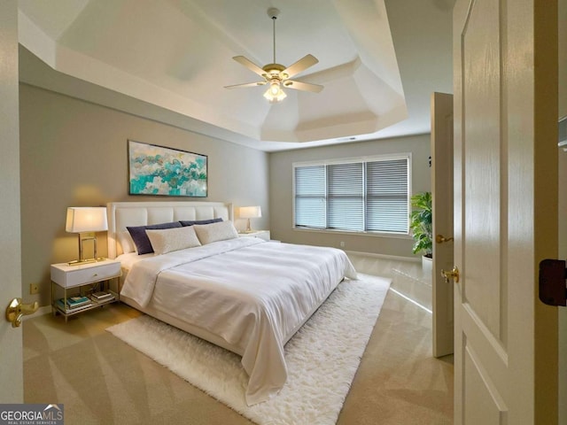 carpeted bedroom featuring a tray ceiling, baseboards, and ceiling fan