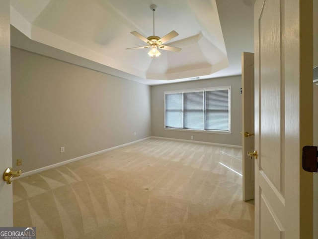 interior space with a tray ceiling, light colored carpet, baseboards, and ceiling fan