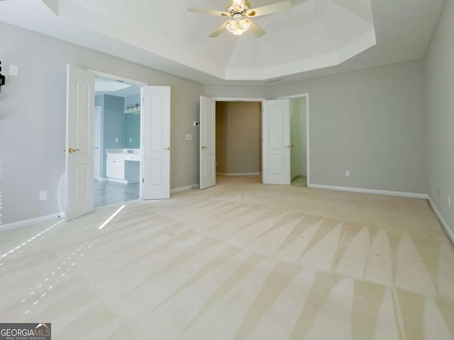 unfurnished bedroom with baseboards, a raised ceiling, light carpet, and ensuite bath