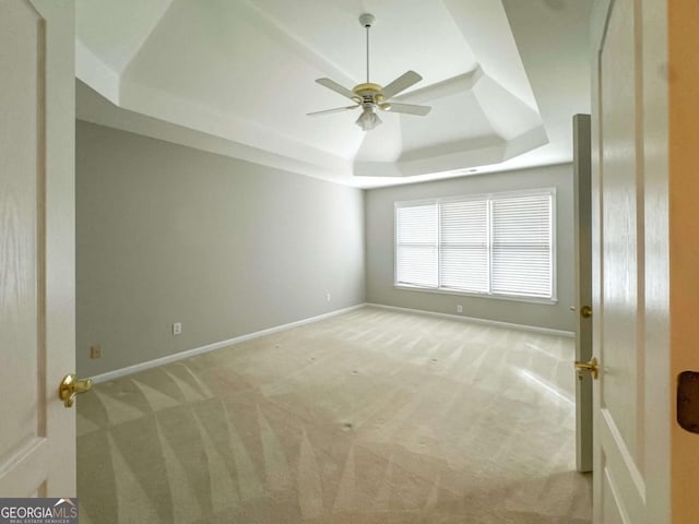 spare room with a raised ceiling, light colored carpet, baseboards, and ceiling fan