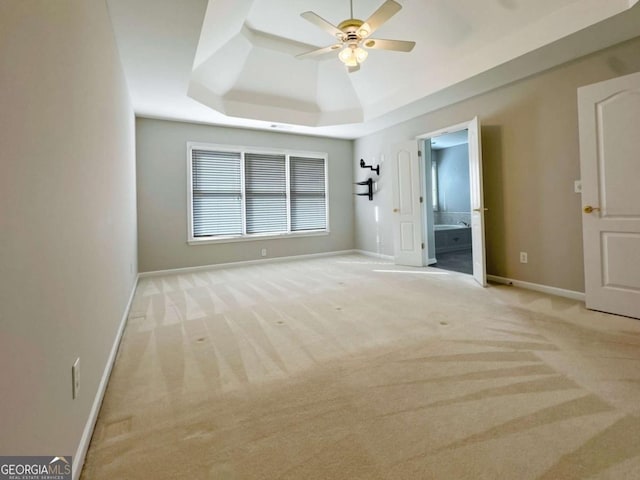 unfurnished bedroom featuring baseboards, a tray ceiling, carpet flooring, ensuite bath, and a ceiling fan