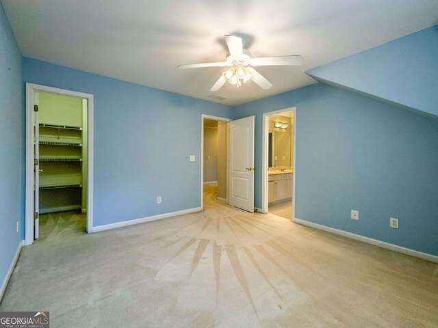 unfurnished bedroom with a spacious closet, light carpet, baseboards, and a ceiling fan