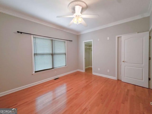 unfurnished bedroom featuring visible vents, a walk in closet, baseboards, crown molding, and light wood-style floors