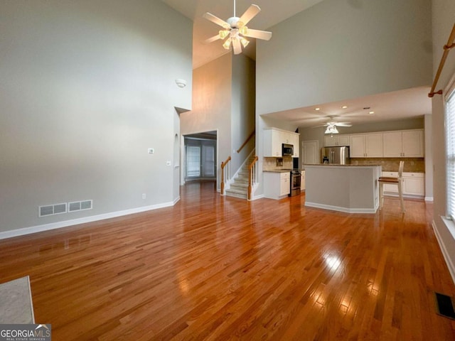 unfurnished living room with stairway, light wood-style flooring, a ceiling fan, and visible vents