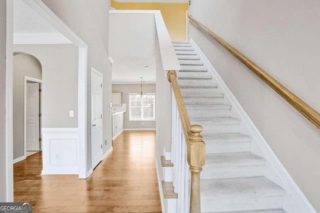 stairway featuring wainscoting, a notable chandelier, wood finished floors, and crown molding