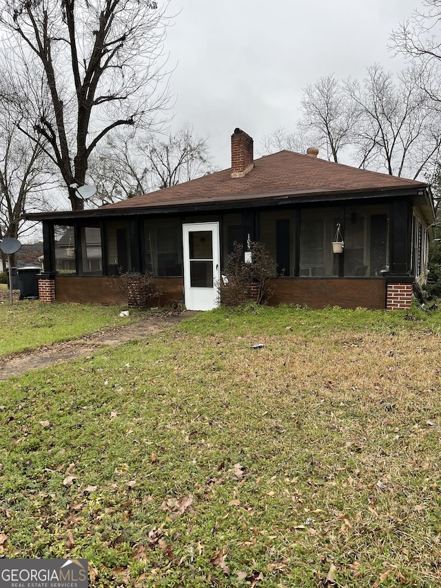 view of front of home featuring a chimney, a front lawn, and a sunroom