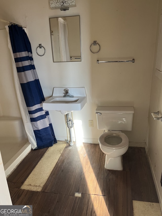 bathroom with a shower with curtain, toilet, a sink, wood finished floors, and baseboards