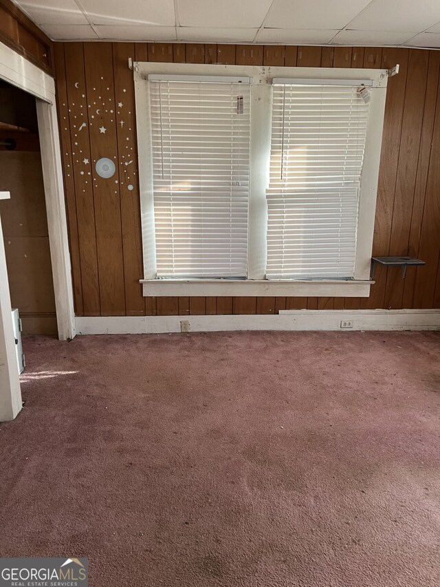 carpeted empty room with a paneled ceiling and wood walls