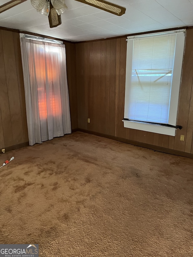 carpeted empty room featuring wooden walls and ceiling fan