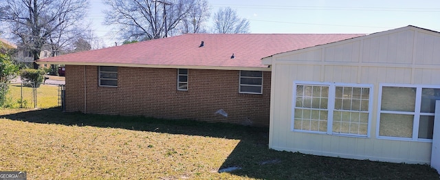 view of home's exterior with brick siding, a lawn, roof with shingles, and fence