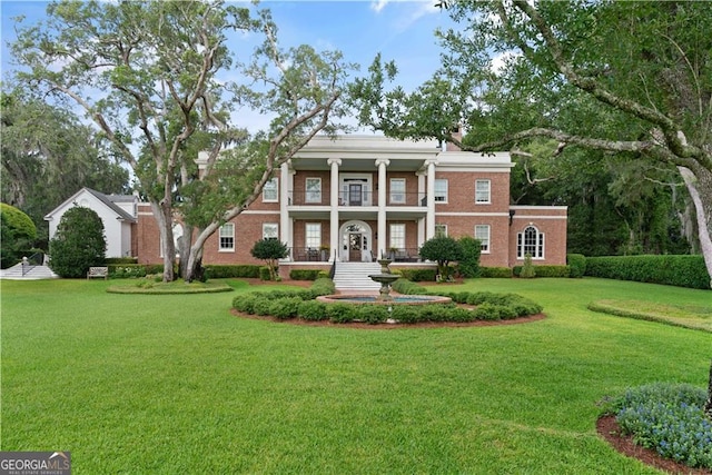 neoclassical home featuring a front lawn, a balcony, and brick siding