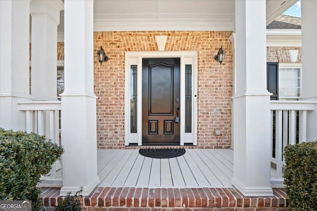 property entrance featuring brick siding, covered porch, and a shingled roof