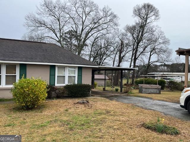 view of front of property with an attached carport, a shingled roof, a front lawn, aphalt driveway, and stucco siding