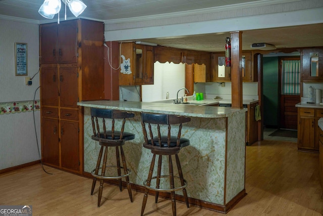 kitchen featuring a sink, brown cabinetry, light wood-style flooring, and crown molding