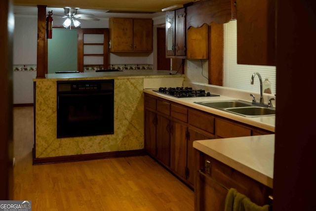 kitchen featuring light wood-type flooring, black appliances, a sink, brown cabinetry, and light countertops