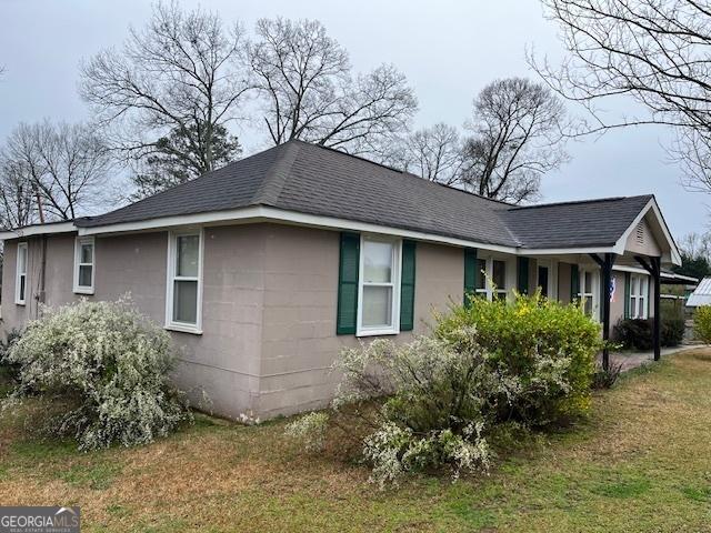 view of home's exterior with concrete block siding, a yard, and roof with shingles