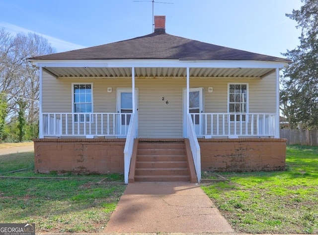 bungalow-style home featuring a porch, a front yard, roof with shingles, and a chimney