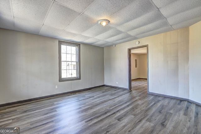 unfurnished room with a paneled ceiling, baseboards, and wood finished floors