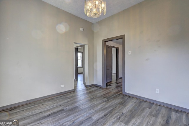 unfurnished room with a textured ceiling, wood finished floors, baseboards, and a chandelier