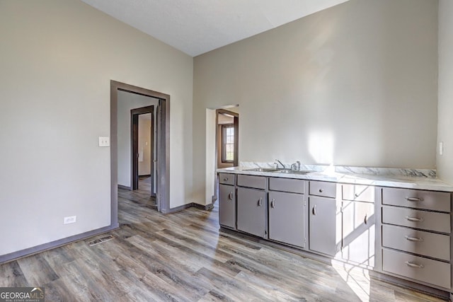 kitchen with light wood finished floors, visible vents, baseboards, light countertops, and a sink