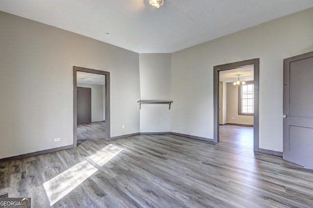 unfurnished room featuring wood finished floors, baseboards, and a chandelier