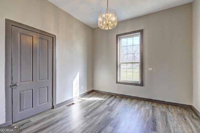 empty room with visible vents, baseboards, wood finished floors, a notable chandelier, and a textured ceiling