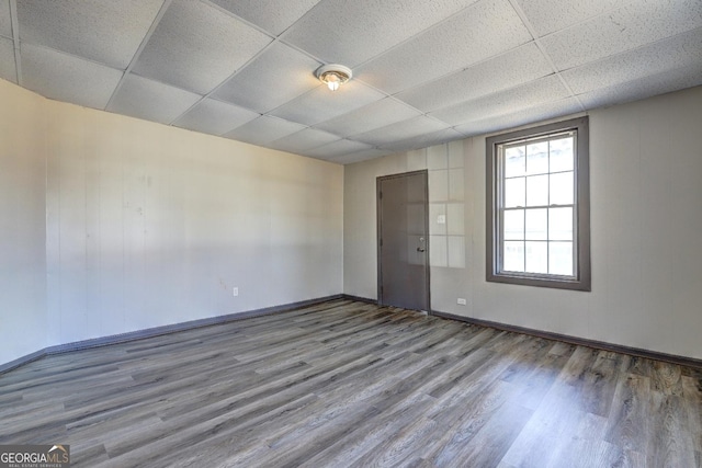 empty room featuring a drop ceiling, baseboards, and wood finished floors