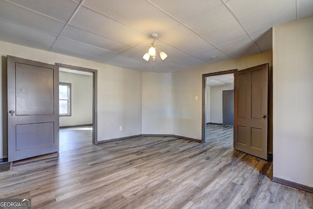 spare room with light wood-type flooring, a paneled ceiling, and baseboards