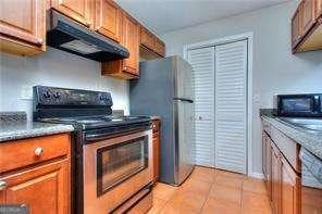 kitchen with under cabinet range hood, light tile patterned floors, brown cabinetry, and appliances with stainless steel finishes