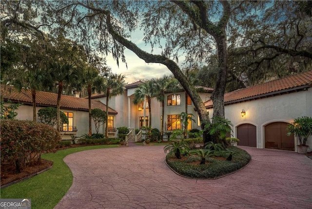 mediterranean / spanish house with curved driveway, a tile roof, a garage, and stucco siding