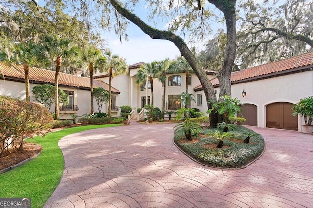 mediterranean / spanish house featuring stucco siding, curved driveway, an attached garage, and a tile roof