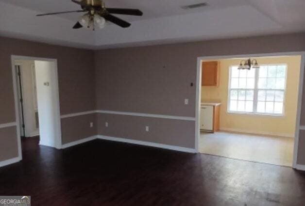 empty room featuring ceiling fan with notable chandelier, wood finished floors, visible vents, and baseboards