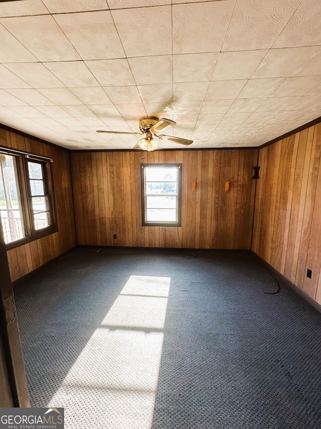 carpeted spare room with ceiling fan and wood walls