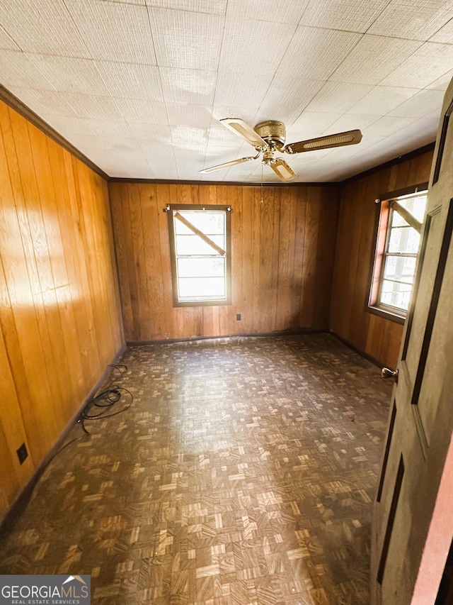 unfurnished room with wooden walls, a healthy amount of sunlight, and a ceiling fan