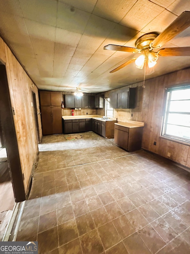 kitchen featuring a ceiling fan, light countertops, a peninsula, and wood walls