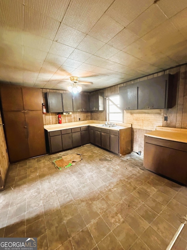 kitchen with light countertops, wooden walls, a ceiling fan, and a sink