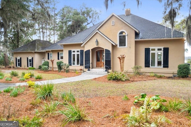 view of front of property featuring a shingled roof, a chimney, and stucco siding