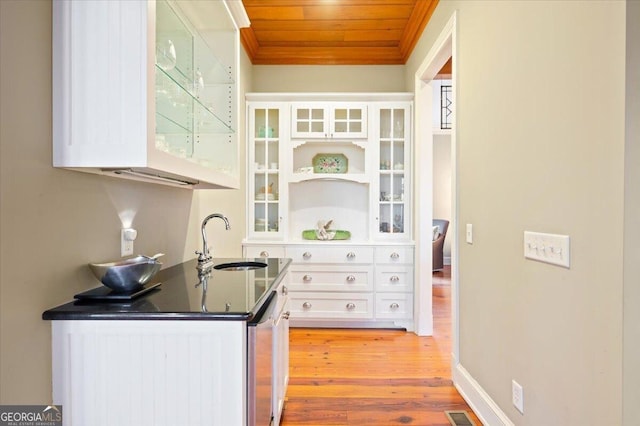 kitchen with a sink, dark countertops, light wood-style floors, white cabinets, and wood ceiling