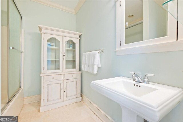 bathroom featuring baseboards, ornamental molding, a sink, tile patterned floors, and combined bath / shower with glass door