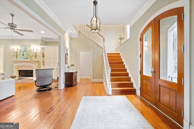 entrance foyer with stairway, a fireplace with raised hearth, ornamental molding, french doors, and light wood-type flooring