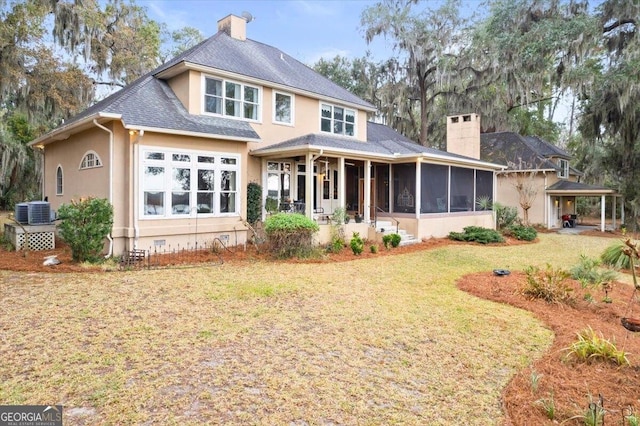 rear view of property featuring a chimney, a yard, and a sunroom