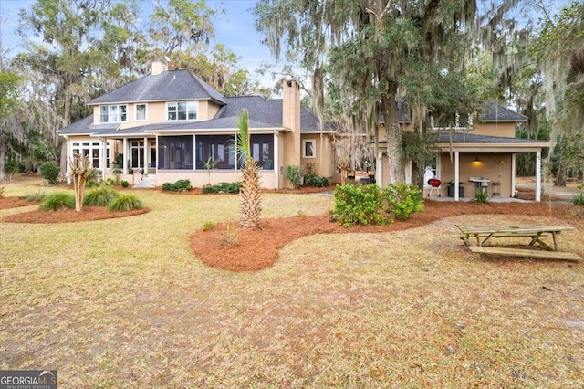 rear view of house with stucco siding, a yard, a sunroom, and a chimney