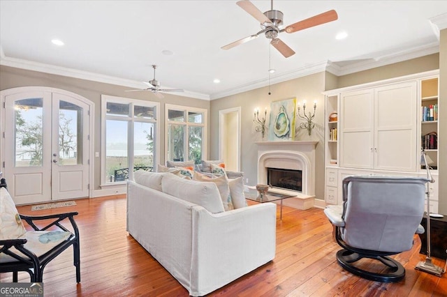 living area featuring crown molding, light wood-style flooring, french doors, and a fireplace with raised hearth