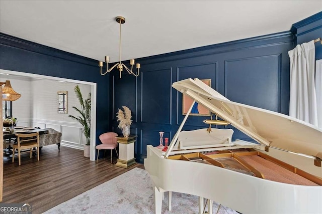 sitting room featuring a decorative wall, crown molding, dark wood finished floors, stairway, and a notable chandelier