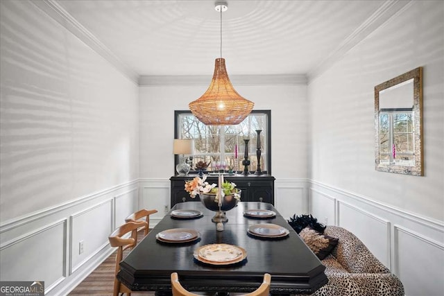 dining room featuring a decorative wall, wainscoting, crown molding, and wood finished floors