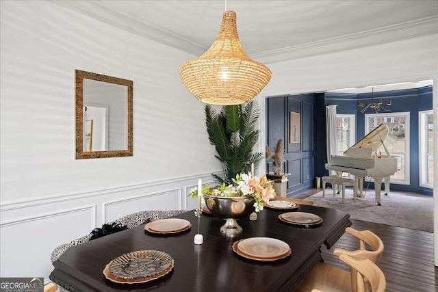 dining room featuring wood finished floors, wainscoting, crown molding, and a decorative wall
