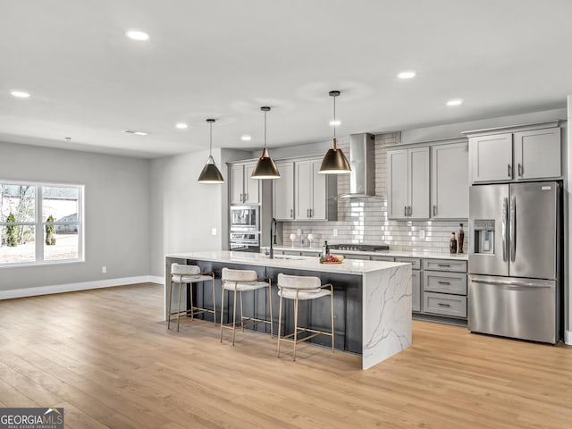 kitchen with wall chimney range hood, gray cabinets, stainless steel appliances, a kitchen breakfast bar, and tasteful backsplash